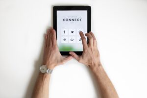Photo of hands holding an iPad with social media apps and the word 'connect' on it by NordWood Themes on Unsplash